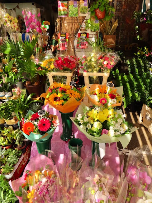 A display of fresh floral bouquets arranged in various sizes and colors at a florist shop. The bouquets include vibrant pink, yellow, orange, and white flowers, wrapped in colorful tissue paper and pl