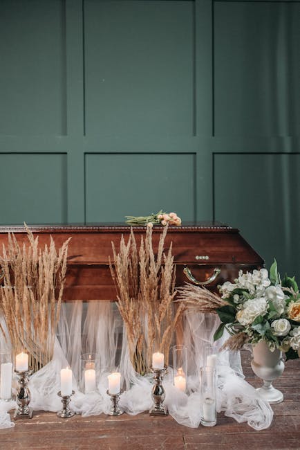 A floral arrangement featuring a bouquet of soft pink roses and white blooms, resting atop a polished wooden piano with a dark green paneled wall in the background. Surrounding the piano are tall, fea